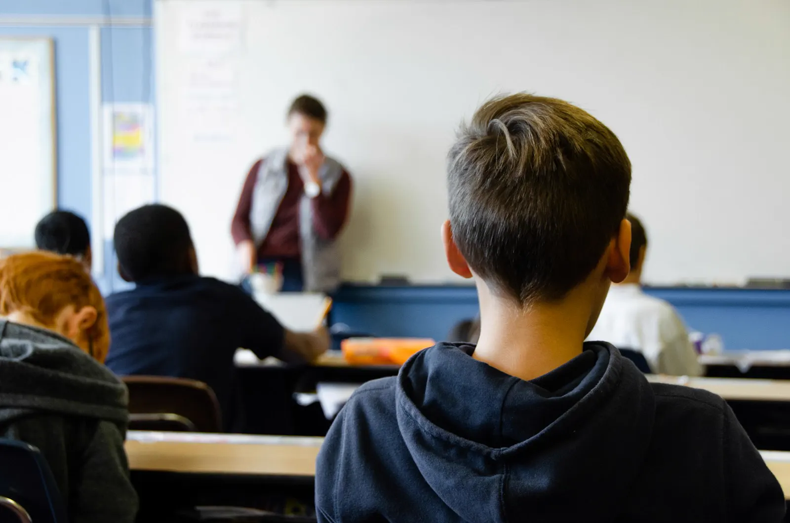 Alumnos de espaldas atendiendo a la profesora en un aula