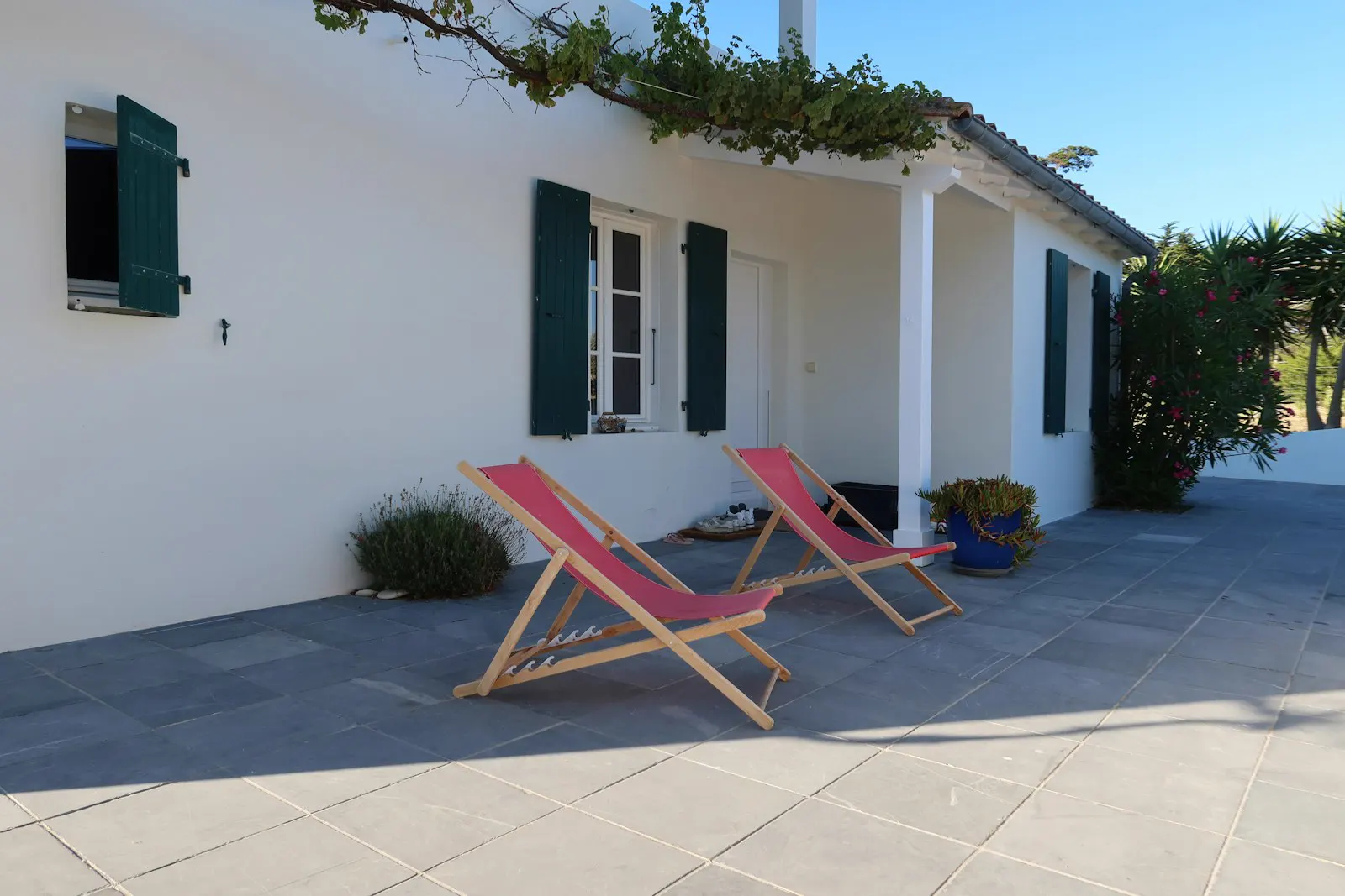 Casa encalada con contraventanas verdes y tumbonas al sol