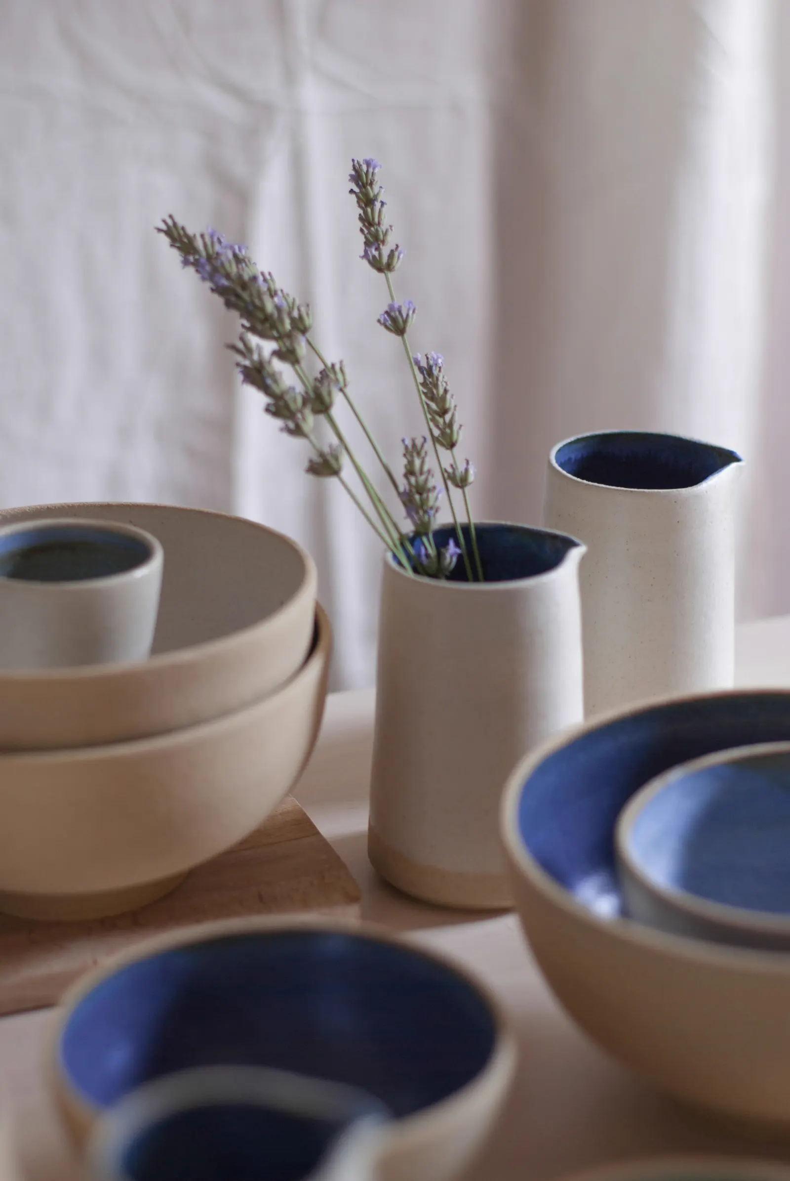 Jarra y cuencos de cerámica con interior azul junto a lavanda